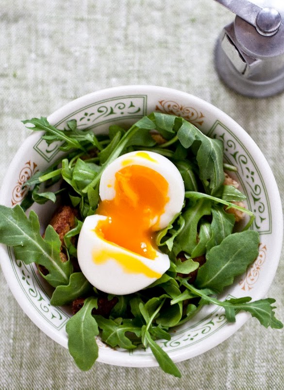 A breakfast salad with soft-boiled eggs, arugula, and toast