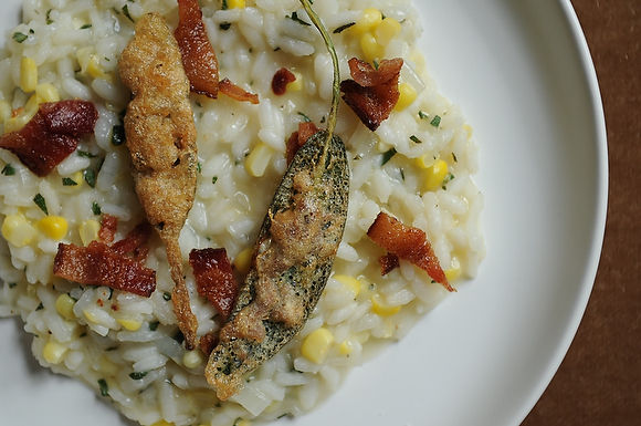 Corn risotto garnished with bacon & anchovy sage leaf bite