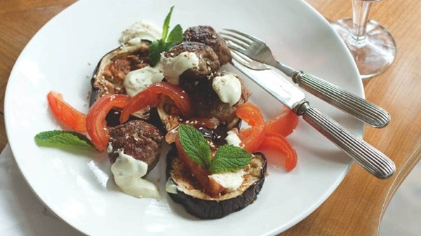 Lamb koftas stuffed with prunes and onions on eggplant and tomatoes with goat's cheese sauce