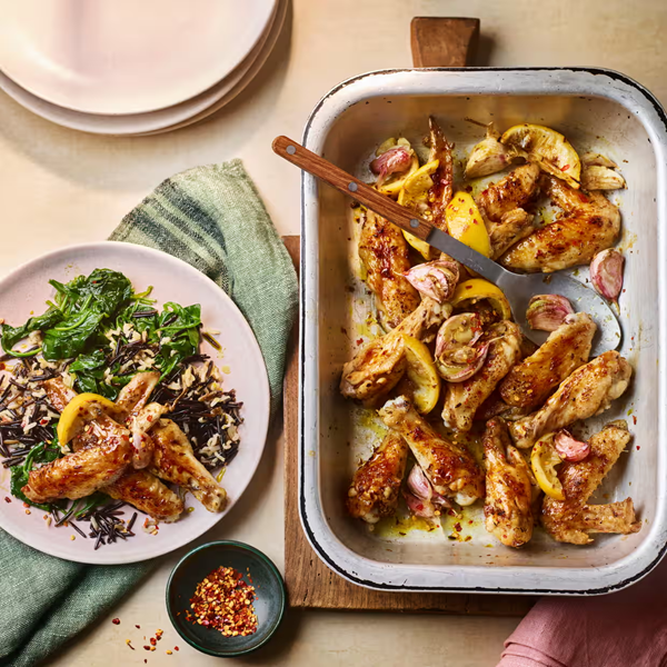 Roast chicken wings with lemon wedges, whole garlic cloves, oregano and cumin