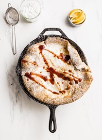 Simple Dutch baby with lemon, powdered sugar and berry jam