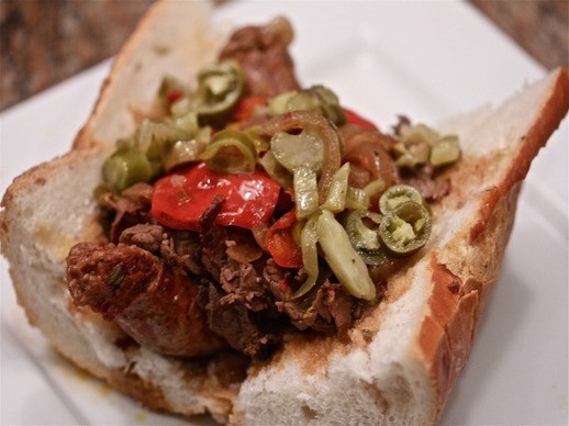 Close up of open-face sandwich with shredded beef, sausage, sliced peppers, and onions. 