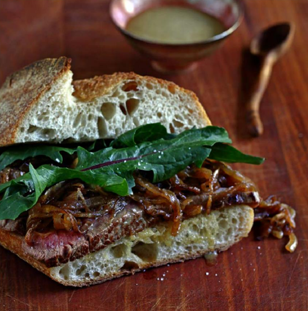 Steak sandwich with caramelized onions, fresh dandelion greens, and wasabi honey spread
