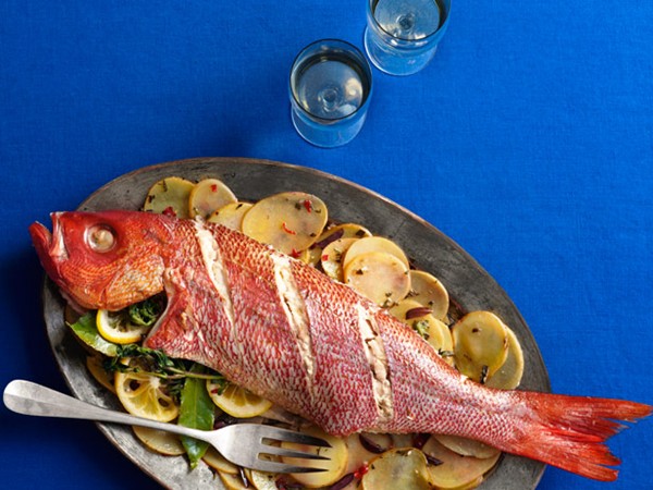 Whole roasted fish with sliced potatoes, olives and herbs